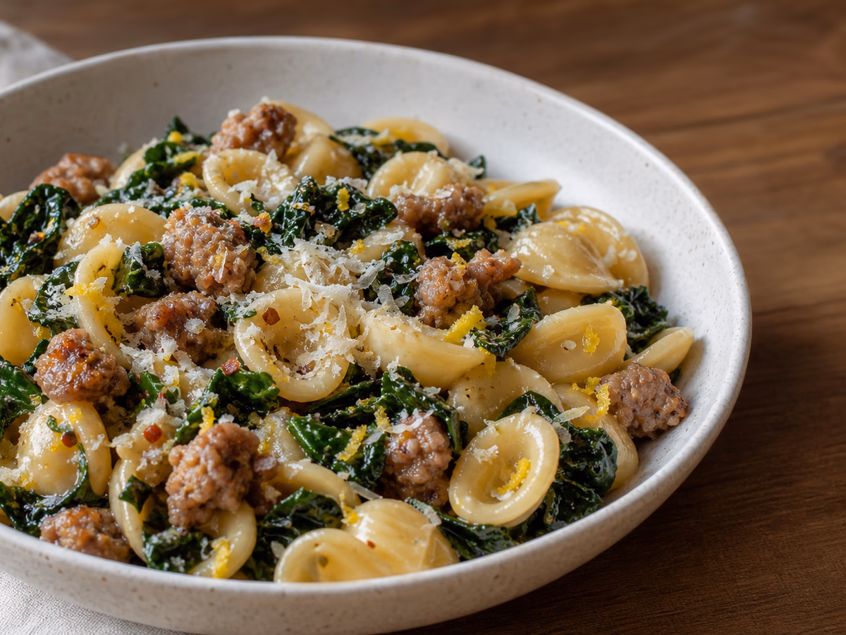 Bowl of short pasta with browned sausage, dark leafy greens, lemon zest, and parmesan