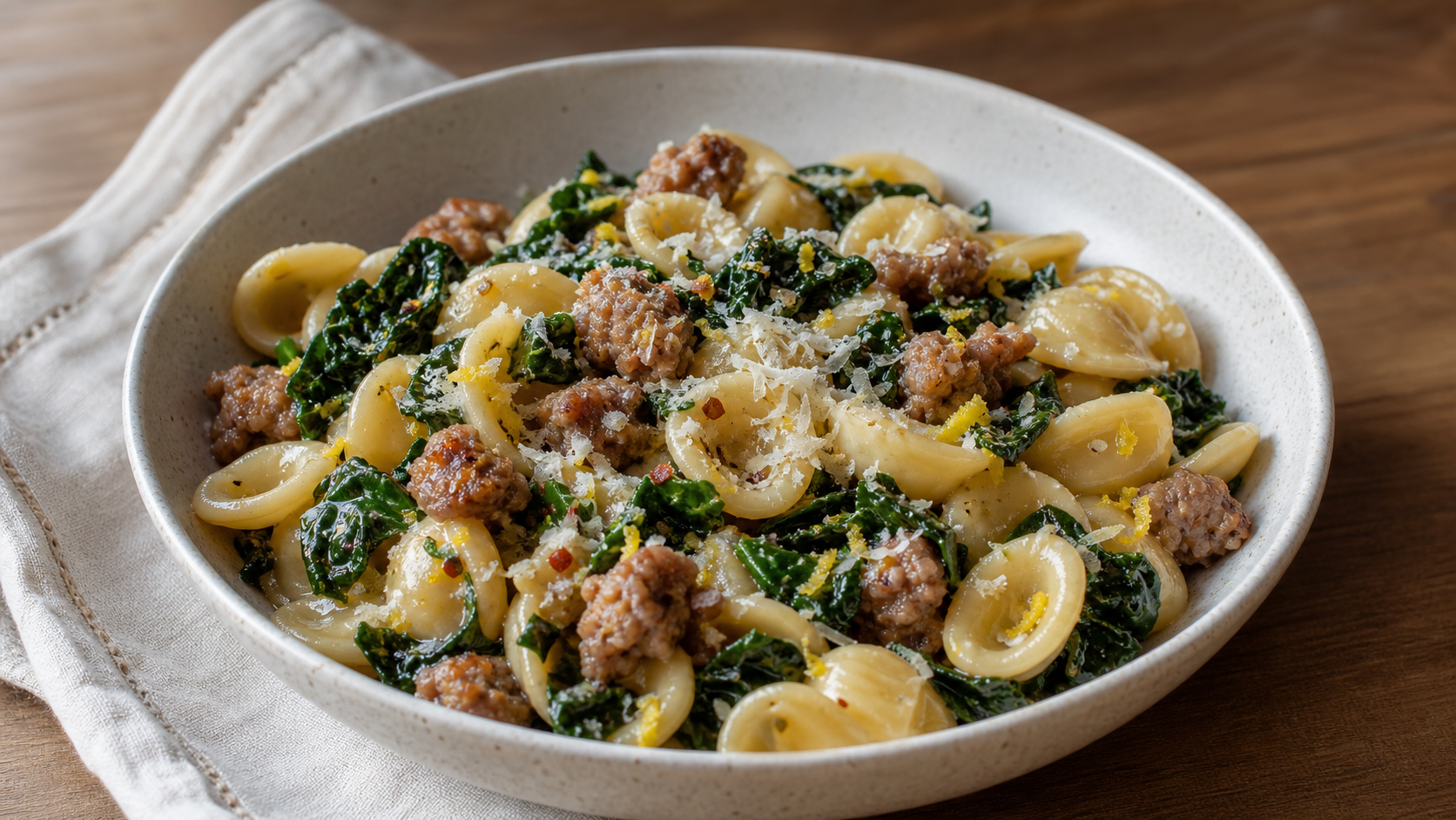 Bowl of short pasta with browned sausage, dark leafy greens, lemon zest, and parmesan